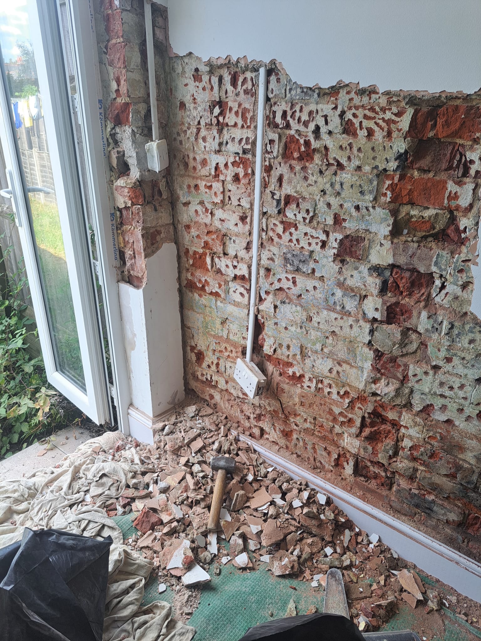 Exposed brickwork and rubble beside a patio door, wall stripped back before damp treatment